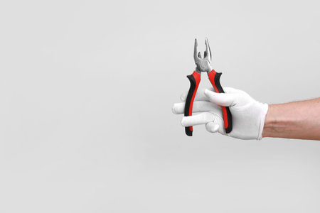 Man's hand in white glove raised holding a black and red tool: pliers, wire cutter. Isolated on white background. Open, clean, ready to cut form. Mock up copy spaceの写真素材