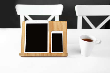 office workplace. a white tablet and a smartphone on a stand on a white table. a mug of tea in the workplaceの写真素材