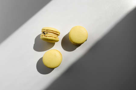 three sweet yellow lemon french macaroons or macarons dessert isolated on white background with light rays from window.の写真素材
