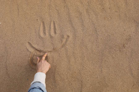 Hand Drawing a Beautiful Cute Smile in Desert Sand - Background.の写真素材