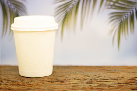 a coffee cup take home on wood on blurred palm leaf background