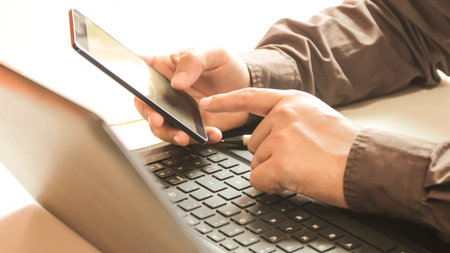 Hands using laptop and smartphone for online shopping with daytime soft light shining high contrastの写真素材