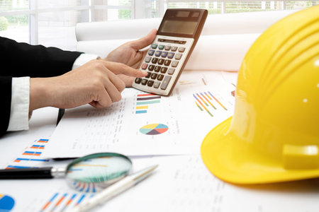 Architect or engineer working project accounting with graph and construction helmet in office,...