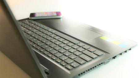 Close up detail side view of a laptop computer keyboard and smartphone with the daytime soft light...