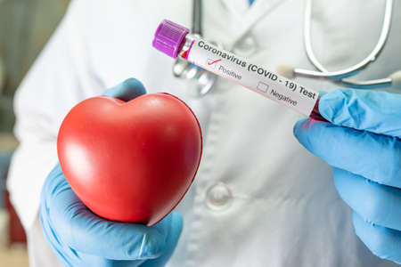 Positive blood infection sample in test tube for covid-19 coronavirus in lab. Scientist holding red heart to encourage patient in hospital.の写真素材