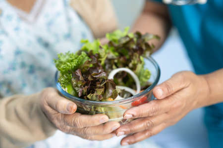Asian senior or elderly old lady woman patient eating breakfast vegetable healthy food with hope and happy while sitting and hungry on bed in hospital.の写真素材