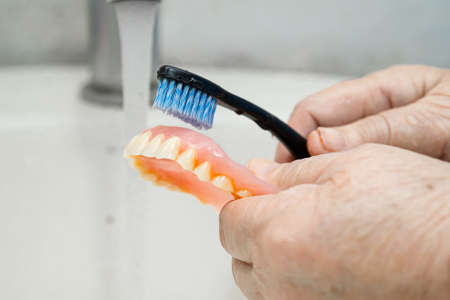Asian senior or elderly old woman patient use toothbrush to clean partial denture of replacement teeth.の写真素材