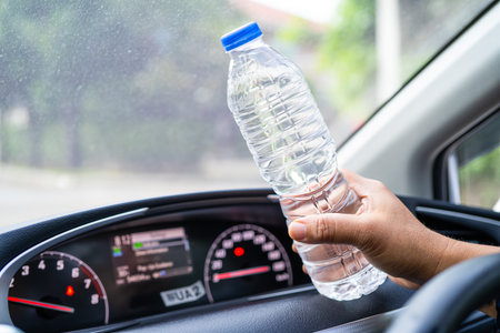 Asian woman driver holding bottle for drink water while driving a car. Plastic hot water bottle...