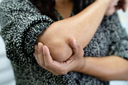 Asian middle-aged lady woman patient touch and feel pain her elbow and arm, healthy medical concept.の写真素材