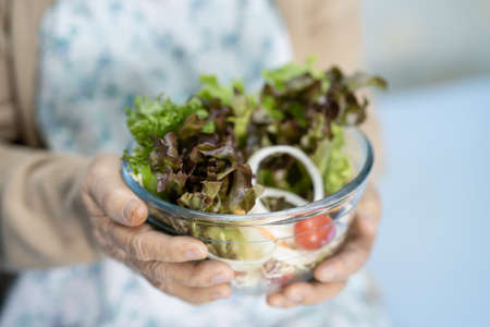 Asian senior or elderly old lady woman patient eating breakfast vegetable healthy food with hope and happy while sitting and hungry on bed in hospital.の写真素材