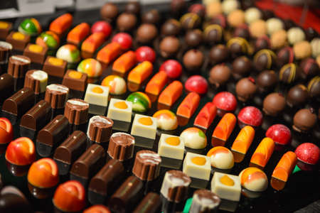 Rows of colorful chocolate pralines on a dark trayの写真素材