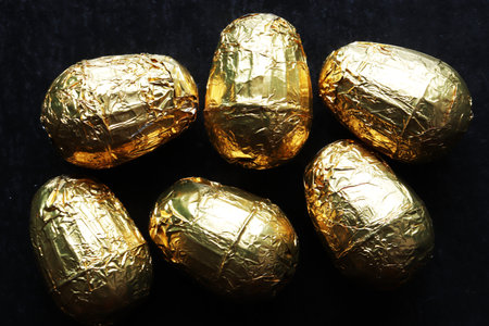 Photography of six chocolate easter eggs wrapped in gold foil on slate background for food illustrationsの写真素材