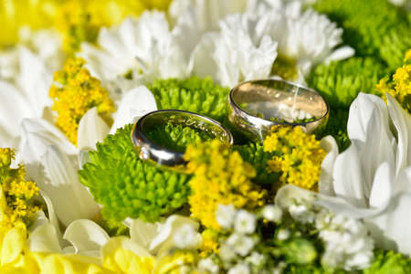 Silver wedding rings of white gold laid on a yellow-white wedding bouquet of meadow flowersの写真素材