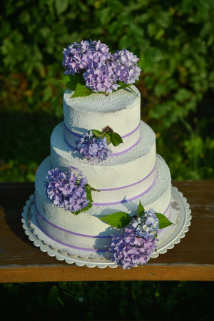 A photo of a wedding cake with violet colored flowers hydrangeas.