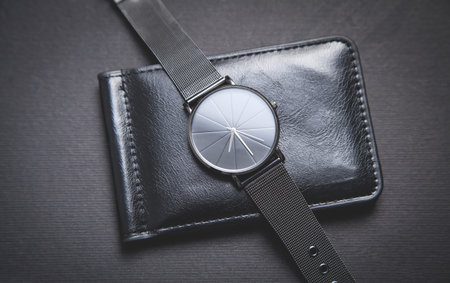 Black wristwatch and wallet on the black background.