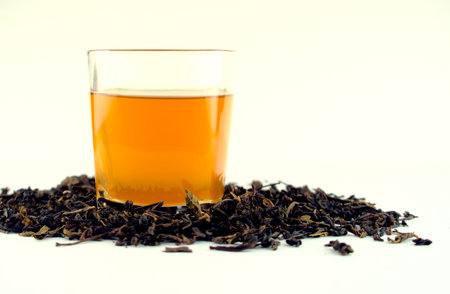 Hot golden, yellow tea in a clear white glass with dried tea leaves isolated on white background. Any hot tea beverage concept.の写真素材