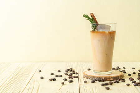pouring milk in black coffee glass with ice cube, cinnamon and rosemary