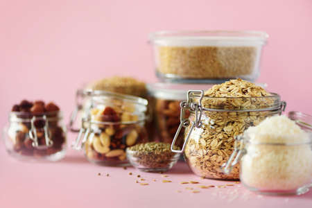 Vegan health food over pink background with copy space. Nuts, seeds, cereals, grains in glass jars. Antioxidants, omega 3, protein and dietary fiber concept.の写真素材