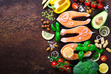Uncooked salmon fish fillet with aromatic herbs, onion, avocado, broccoli, pepper bell, vegetables on wooden background, top view. Ingredients for cooking on background.の写真素材
