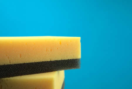 Yellow combined black scouring pad sponges isolated with blue background. Household, kitchen, vehicles clean stuff or any cleaning concept. Off-center, head on composition. Horizontal style and space.の写真素材