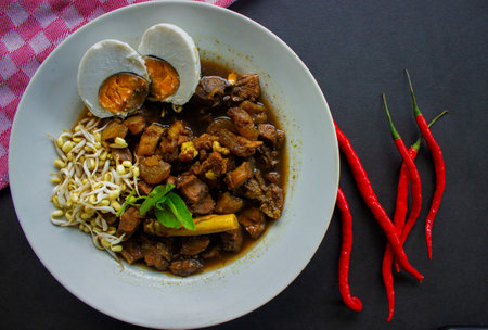 Rawon or Nasi Rawon/Rawon Rice is traditional Indonesian beef black soup served with sprouts, salted eggs, kluwek seasoning. From east java. Isolated on black backgroundの素材