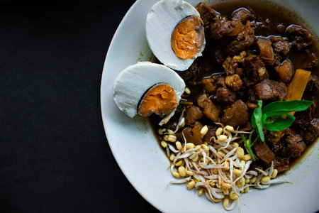 Rawon or Nasi Rawon/Rawon Rice is traditional Indonesian beef black soup served with sprouts, salted eggs, kluwek seasoning. From east java. Isolated on black backgroundの素材