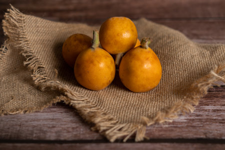 group of organic nisperos on a raffia cloth on a wooden tableの素材