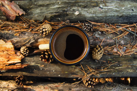 Yellow metal cup with hot coffee on the wooden background with the coins, needles and bark of tree, top view.の素材