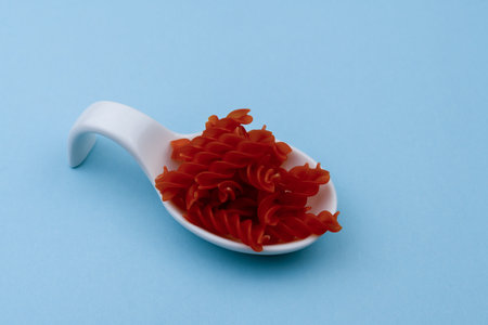white ceramic spoon with red spiral macaroni and blue backgroundの素材