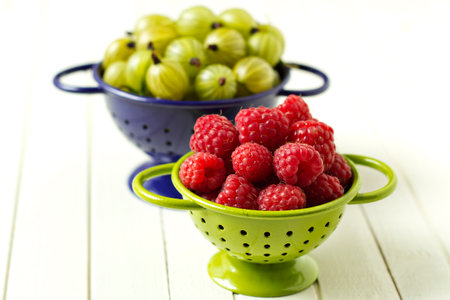 Fresh gooseberries and raspberries in colanders, summer berriesの素材