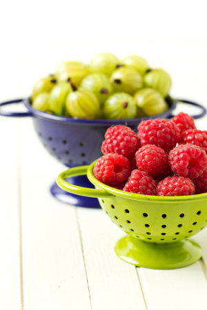Fresh gooseberries and raspberries in colanders, summer berriesの素材