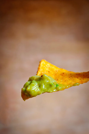 Nacho chips with guacamole dip on a wooden background
