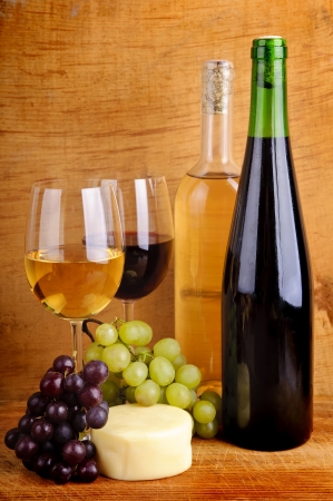 still life with cheese, grapes, red and white wine in bottles and glasses on a wooden backgroundの写真素材