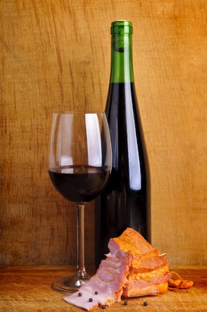 still life composition with glass and bottle of red wine and smoked ham on a vintage wooden backroundの写真素材