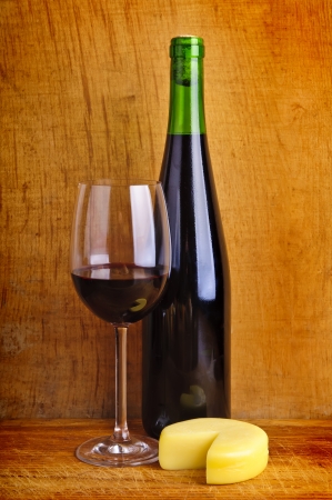 glass and bottle of red wine with cheese on a wooden backgroundの写真素材