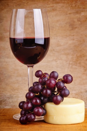 still life with glass of red wine, grapes and cheese on a wooden vintage backgroundの写真素材