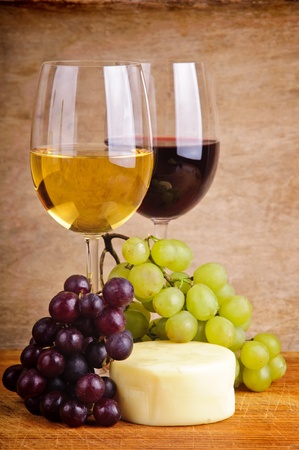 still life composition with red and white wine, grapes and cheese on a wooden vintage backgroundの写真素材