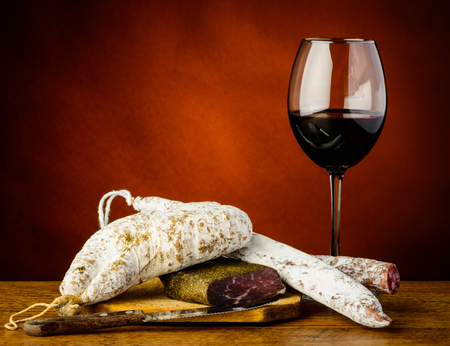 glass of red wine and traditional sausages on a wooden plateの写真素材