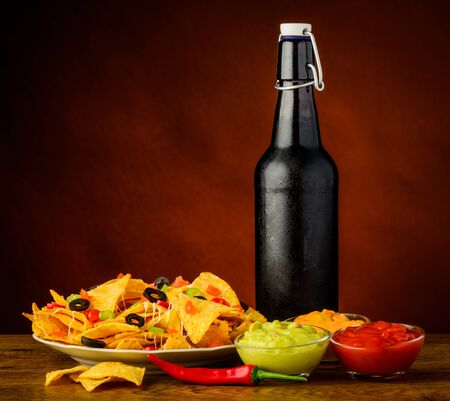 tortilla chips with cheese, salsa and guacamole dip and bottle of beerの写真素材