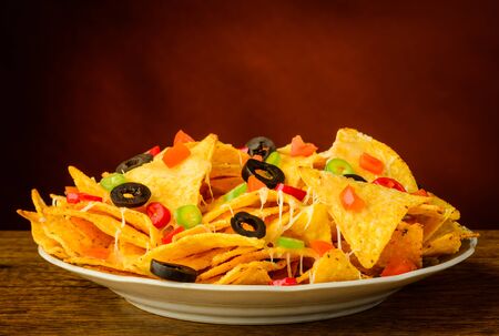 nachos tortilla chips with cheese, olives and chili peppers on a plateの写真素材