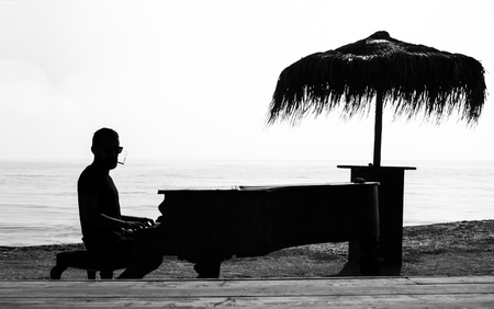 Man with sunglasses and cigarette in his mouth playing classic piano on a beachの写真素材