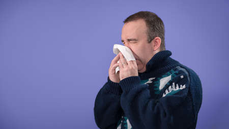 A sick man or a man with allergies is blowing his nose, with copyspace for textの写真素材