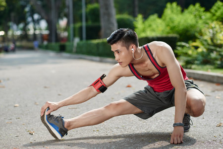 Asian young jogger stretching legs outdoors