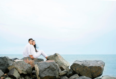 Young couple sitting on rocks and looking at the seaの写真素材