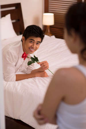 Portrait of young Asian man with rose lying on bed and looking at his girlfriend の写真素材