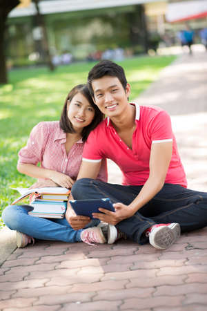 Happy college couple sitting on the ground in campusの写真素材