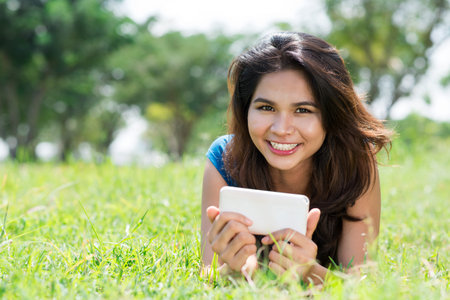 Portrait of a pretty girl lying on the lawn and texting