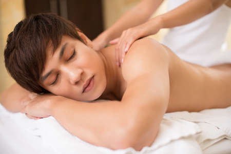 Relaxed guy receiving spa treatment which relieves shoulder tensionの写真素材