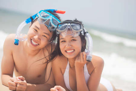 Smiling couple with goggles looking at camera on the beachの写真素材