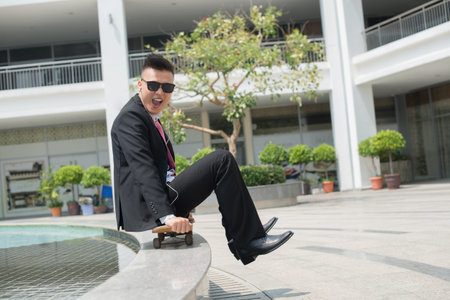 Portrait of a trendy business guy sitting on skateboard holding his legs above the ground